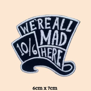 May include: Black and white embroidered iron-on patch featuring a hat with the text "We're all mad here" and "10/6" inside the hat. The patch measures 6 cm by 7 cm.