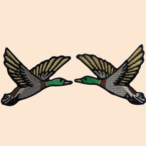 May include: Two embroidered flying ducks with brown wings and green heads.