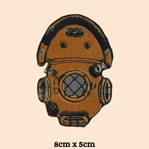 May include: An embroidered patch of a vintage diving helmet in brown and black. The patch measures 8 cm by 5 cm.