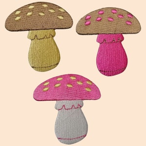May include: Three embroidered mushroom patches. One mushroom is brown with yellow spots and a yellow stem. Another mushroom is brown with pink spots and a pink stem. The last mushroom is pink with gold spots and a gray stem.