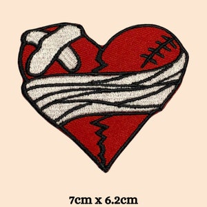 May include: A red heart-shaped patch with a white bandage wrapped around it. The heart is cracked and stitched with black thread. The patch measures 7 inches by 6.2 inches.