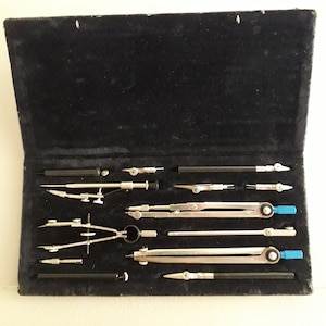 Könnte beinhalten: Ein Set von Zeichenwerkzeugen, darunter Zirkel und Reißfedern, in einem schwarz samtgefütterten Etui. Die Werkzeuge sind silberfarben mit schwarzen und blauen Akzenten. Für präzises Zeichnen und Messen.