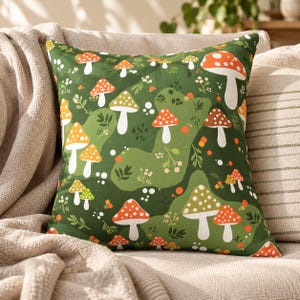 Op de afbeelding: Een vierkant sierkussen met een donkergroene achtergrond en een herhalend patroon van diverse paddenstoelen in tinten oranje, rood, wit en bruin, afgewisseld met kleine witte stippen, groene blaadjes en oranje cirkelvormige accenten.