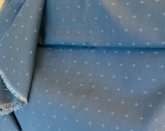 May include: A folded piece of blue fabric with a repeating pattern of small, white floral shapes. The fabric has a slightly textured appearance and a raw, unfinished edge. The material is likely cotton or a similar woven textile.