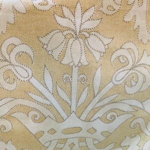 May include: Close-up of a fabric with a repeating floral pattern. The design features off-white floral motifs outlined with a brown rope-like texture against a light yellow background. The pattern includes stylized leaves and flower shapes.
