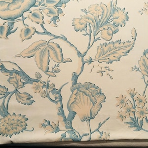 May include: Floral fabric with a cream background and a repeating pattern of stylized flowers and foliage in light blue and beige. The design features large blooms, leaves, and branches, creating a classic, elegant look.