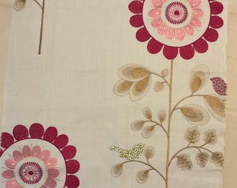 May include: Cream-colored fabric with embroidered floral design. Large flowers in shades of pink and red are featured, along with brown stems and leaves. A small green and white bird is perched on a branch. The fabric has a textured appearance.