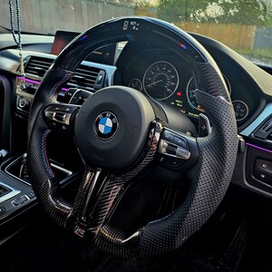 May include: A black leather steering wheel with a carbon fiber trim and a BMW logo. The steering wheel has a digital display showing the speed and other information. The steering wheel has paddle shifters on the back.
