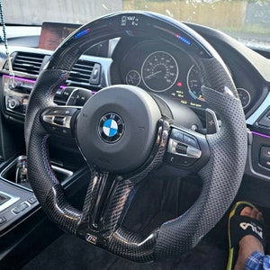 May include: A black leather steering wheel with carbon fiber accents and a perforated grip. The steering wheel has a BMW logo, paddle shifters, and a digital display showing "1647" and "0".