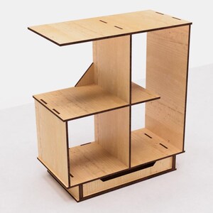 May include: A wooden shelf unit with four compartments and a drawer. The shelf is made of light wood with a natural finish. The drawer is made of the same wood and has a brown finish.