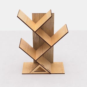 May include: A wooden bookshelf with a tree-like design. The shelves are angled and create a zig-zag pattern. The bookshelf is made of light brown wood and has a natural wood finish.