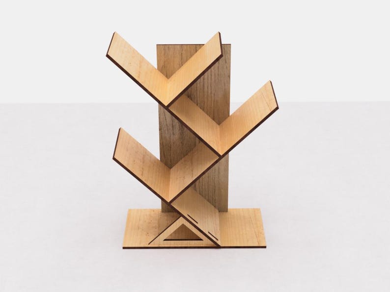 May include: A wooden bookshelf with a tree-like design. The shelves are angled and create a zig-zag pattern. The bookshelf is made of light brown wood and has a natural wood finish.