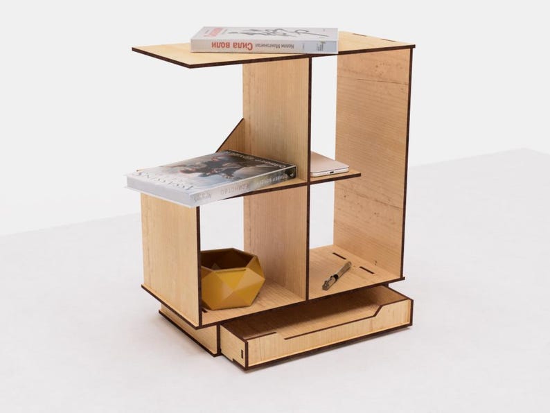 May include: A wooden shelf unit with a drawer, featuring four compartments. The shelf unit is made of light wood with a natural finish. It is decorated with books, a small bowl, and a pen.