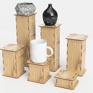 Pu&ograve; includere: Un set di sei alzate in legno per esposizione in una tonalit&agrave; di legno chiaro con un bordo rosso-marrone. Le alzate sono disposte in una formazione sfalsata, con una tazza in ceramica bianca, un vaso in ceramica nero e un vaso in ceramica grigio sulla parte superiore di tre delle alzate.