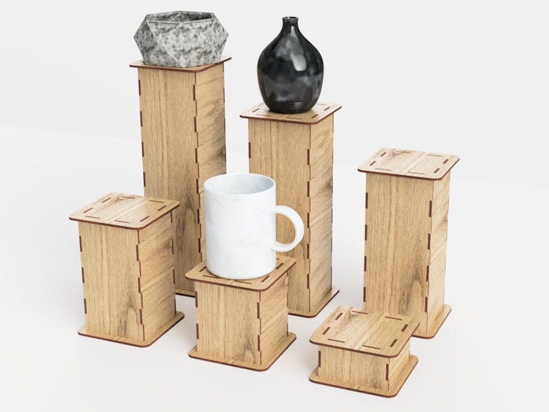 Pu&ograve; includere: Un set di sei alzate in legno per esposizione in una tonalit&agrave; di legno chiaro con un bordo rosso-marrone. Le alzate sono disposte in una formazione sfalsata, con una tazza in ceramica bianca, un vaso in ceramica nero e un vaso in ceramica grigio sulla parte superiore di tre delle alzate.