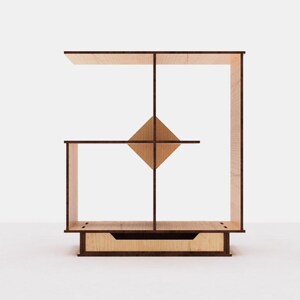 May include: A wooden shelf unit with a geometric design. The shelf has four compartments and a drawer at the bottom. The shelf is made of light brown wood with dark brown accents.
