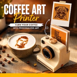 Könnte beinhalten: Ein cremefarbener Kaffee-Art-Drucker in Form einer Vintage-Kamera mit schwarzem und goldenem Objektiv. Daneben steht eine Keramiktasse mit Milchschaum, der mit einem braunen Porträt verziert ist. Darüber zeigt ein Druck einen Mops und den Text BUT FIRST COFFEE.