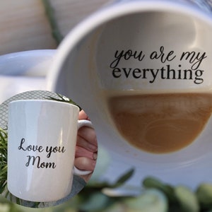 Può includere: Due tazze in ceramica bianca con lettere nere. Una tazza dice "Love you Mom" e l'altra tazza dice "You are my everything".