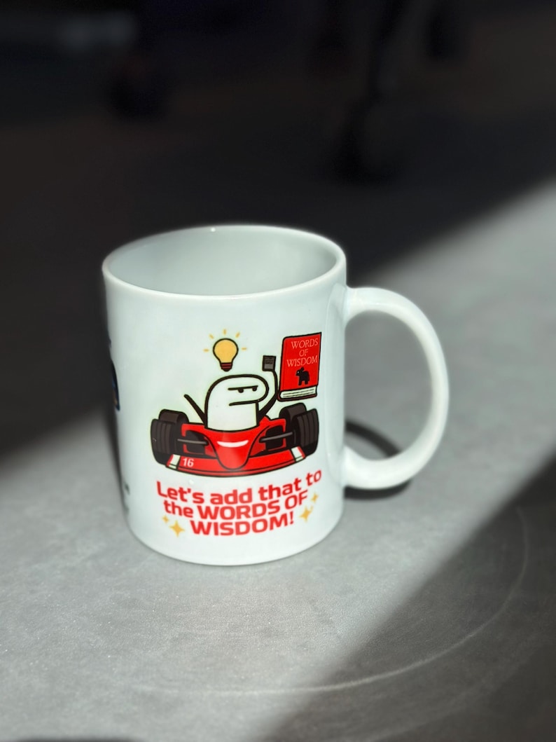 May include: White ceramic mug featuring a cartoon image of a red race car with a stick figure driver holding a book and lightbulb. The mug has the text "Let's add that to the WORDS OF WISDOM!"
