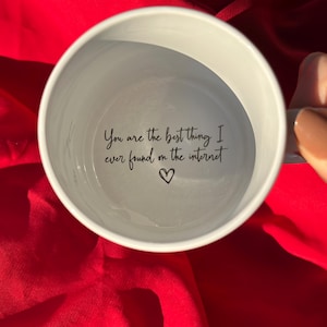 Pode incluir: Caneca de cerâmica branca com o texto "You are the best thing I ever found on the internet" e um símbolo de coração. A caneca é segurada contra um fundo vermelho.