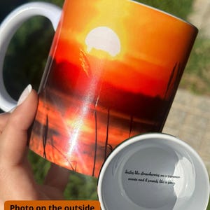Könnte beinhalten: Eine weiße Keramiktasse mit einer Sonnenuntergangsszene auf der Außenseite. Die Innenseite der Tasse hat ein Zitat, das lautet "Tastes like strawberries on a summer evening and it sounds like a song."