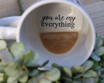 May include: White ceramic coffee mug with the text "you are my everything" printed on the inside. The mug is filled with coffee.