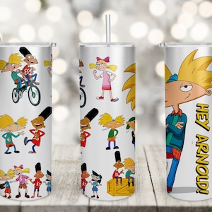 Puede incluir: Tres vasos de acero inoxidable con diferentes diseños que presentan personajes de la serie de televisión animada Hey Arnold! El primer vaso tiene un patrón repetitivo de Arnold y sus amigos. El segundo vaso tiene un patrón repetitivo de Arnold y sus amigos. El tercer vaso presenta una imagen grande de Arnold con el texto "Hey Arnold!" en letras amarillas.