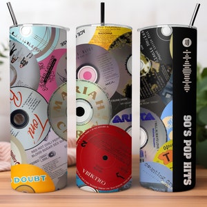 May include: Three stainless steel tumblers with different designs featuring a collage of 90s pop music CDs. The first tumbler has a colourful collage of CDs with the text "DOUBT" on the bottom. The second tumbler has a red CD with the text "COLUMBIA" on the bottom. The third tumbler is black with a white Spotify logo and the text "90's POP HITS".