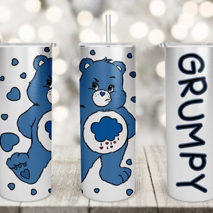 May include: Three stainless steel tumblers with a white background and blue Care Bear designs. The tumbler on the left has a blue Care Bear with a grumpy expression and a blue heart on its foot. The tumbler in the middle has a blue Care Bear with a grumpy expression and a blue cloud with rain drops. The tumbler on the right has the word "GRUMPY" written vertically in black.