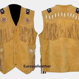 May include: A tan suede vest with fringe detailing, decorative beading, and pockets. The vest features a V-neck and button closure. The back of the vest also has fringe and decorative cutouts. The vest is a traditional style.