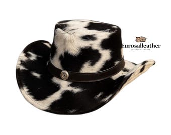 Puede incluir: Sombrero de vaquero con un patrón de manchas blancas y negras. Cuenta con una banda de cuero marrón oscuro con un botón plateado. El ala del sombrero es curvada y tiene una forma clásica de vaquero. El logotipo "Eurosalleather" es visible.