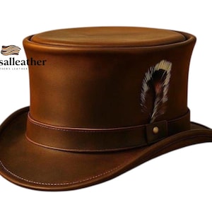 Puede incluir: Un sombrero de copa de cuero marrón con un adorno de pluma. El sombrero tiene un ala ancha, una banda alrededor de la copa y una pluma decorativa en el lateral. El sombrero tiene el texto "Eurosalleather".