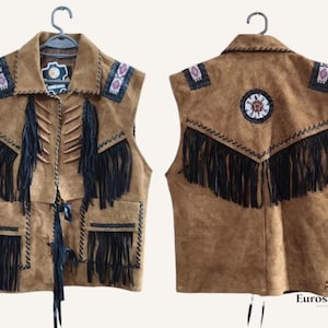 Puede incluir: Un chaleco de ante marrón con flecos negros y abalorios decorativos. El chaleco presenta un cuello, bolsillos y un diseño detallado en la espalda. El chaleco se muestra en una percha.