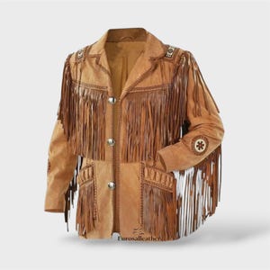 Puede incluir: Una chaqueta de ante color tostado con largos flecos en el pecho, mangas y bolsillos. La prenda incluye tres botones plateados, costuras decorativas y detalles circulares estampados en los hombros y las mangas.