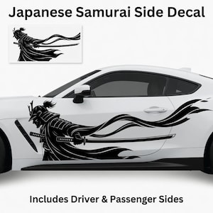 May include: A black vinyl car decal featuring a Japanese samurai warrior in traditional armor holding a katana sword. The design includes flowing fabric elements extending horizontally across the side of a white vehicle. Text reads Japanese Samurai Side Decal.
