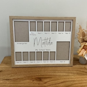 May include: A rectangular light wood photo frame with a white mount featuring multiple cutouts for school photos. The mount is printed with the name Matilda, the text My School Years, and labels for school years from Kindergarten through to Year 12.