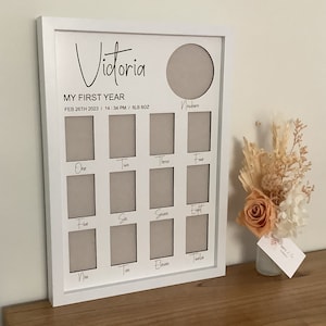 May include: A white framed baby milestone photo display, featuring the name "Victoria". It has spaces for photos from newborn to twelve months. The frame also includes the baby's birthdate, time, and weight: 8lb 6oz.