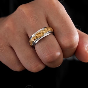 May include: A silver and gold ring with a dragon design. The ring features a detailed gold dragon wrapped around a silver band. The dragon's scales and features are clearly visible, creating a striking piece of jewelry.