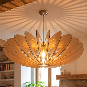 Könnte beinhalten: Ein holzfarbener Kronleuchter in Blütenform hängt über einem Wohnzimmer mit Kamin. Die Leuchte besteht aus geschichtetem, hellfarbenem Holz. Der Raum verfügt über ein beiges Sofa, einen Holztisch und einen Steinkamin mit Feuer.