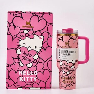 May include: Pink Stanley Quencher H2.0 tumbler and matching box featuring Hello Kitty and heart designs. The tumbler has a handle and a clear lid. The box and tumbler have the text "Hello Kitty" and "Stanley".