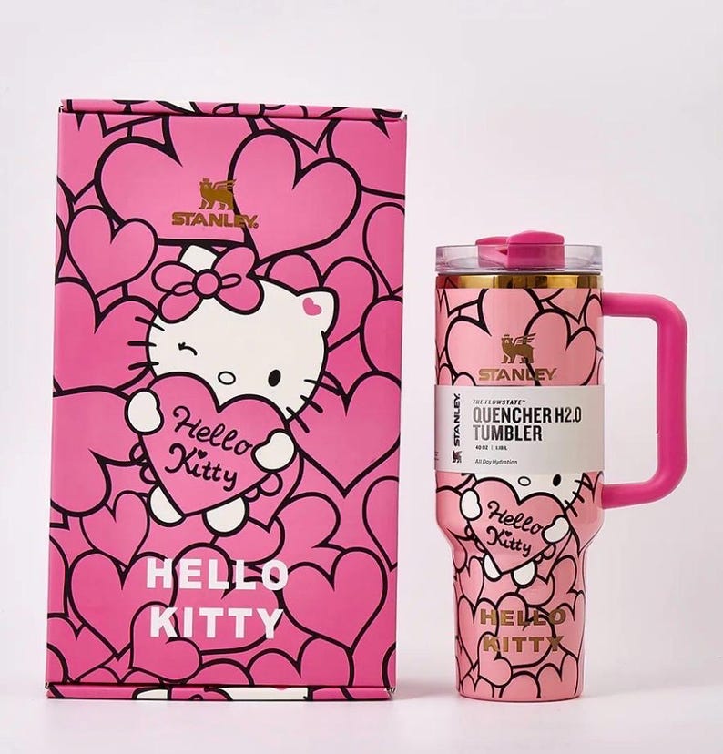 May include: Pink Stanley Quencher H2.0 tumbler and matching box featuring Hello Kitty and heart designs. The tumbler has a handle and a clear lid. The box and tumbler have the text "Hello Kitty" and "Stanley".