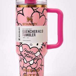 May include: Pink Stanley Quencher H2.0 tumbler with a Hello Kitty design. The tumbler has a pink handle and lid, and features a heart pattern. The tumbler holds 40 oz (1.18 L) and has the text "Hello Kitty" on the front.