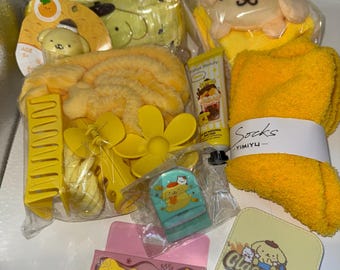 Op de afbeelding: Een verzameling gele schoonheids- en badproducten, waaronder een pluche speelgoed, haaraccessoires, een handdoek en een kleine cosmeticale tube. De items zijn verpakt in doorzichtig plastic en hebben cartoonkarakterontwerpen.