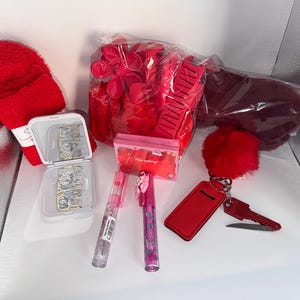 Puede incluir: Una colección de accesorios rojos, que incluye un par de calcetines afelpados, pinzas para el pelo, un llavero con pompón y bolígrafos. También incluye una funda transparente con pegatinas y una pequeña bolsa rosa con cremallera.