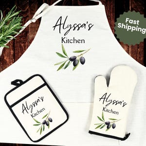 May include: White kitchen apron, pot holder, and oven mitt set. Each item features the text "Alyssa's Kitchen" in script, along with a watercolor olive branch design. The apron has a neck strap and waist ties.