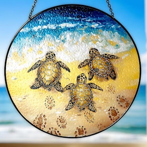May include: A stained glass window hanging features three sea turtles swimming in a blue and yellow ocean scene. The turtles are brown and green with black eyes and are swimming in a sandy bottom with footprints.