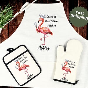 May include: A white kitchen apron, oven mitt, and pot holder set. Each item features a pink flamingo wearing a chef's hat and holding a whisk, with the text "Queen of the Flockin' Kitchen" and a name. The set is designed for cooking.