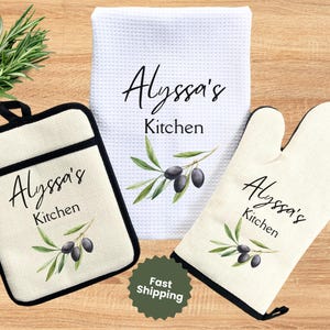 May include: A kitchen set featuring a pot holder, oven mitt, and a white waffle-weave towel. Each item is cream-colored and adorned with the text "Alyssa's Kitchen" and a watercolor olive branch design. The pot holder and oven mitt have black trim.