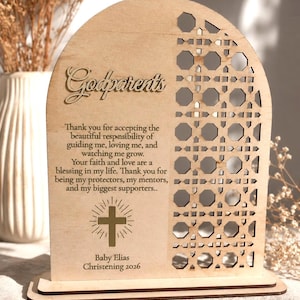 May include: An arched wooden plaque featuring a laser-cut geometric pattern on the right side. The text reads: Godparents, Thank you for accepting the beautiful responsibility of guiding me, loving me, and watching me grow. Baby Elias Christening 2026.