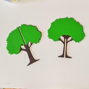 May include: Two flat, tree-shaped cutouts featuring a vibrant green canopy and a dark brown trunk. Each tree has a vertical slit running from the top of the canopy down through the centre of the trunk, allowing the two pieces to interlock.